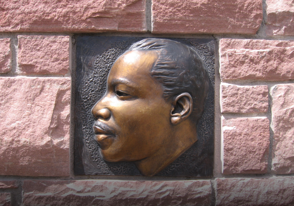 Close-up of a bronze relief plaque depicting Dr. Martin Luther King Jr.'s profile, set into a red sandstone pillar, showing its cleaned and repaired patina.