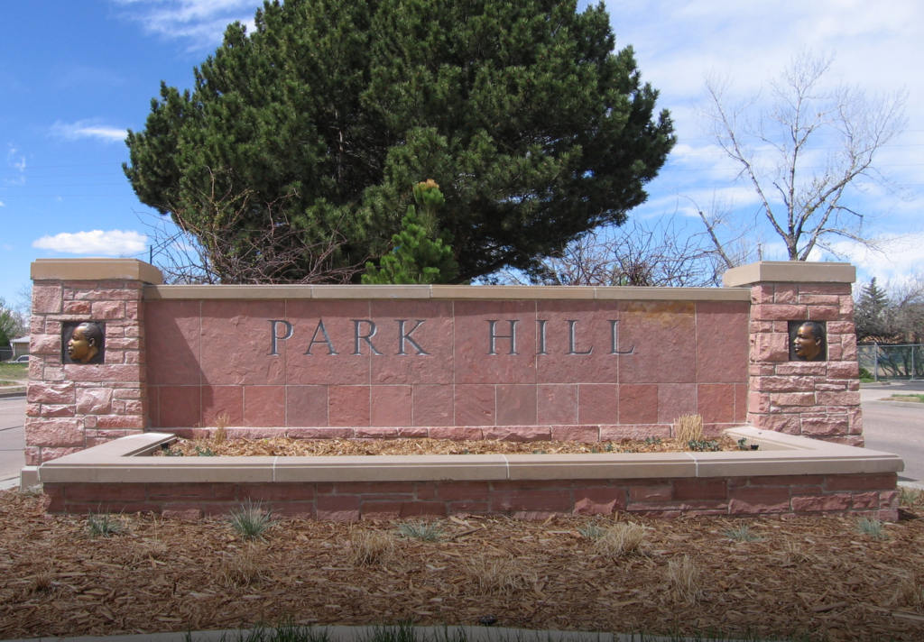 A red sandstone "Park Hill" neighborhood monument sign flanked by two stone pillars, each inset with a bronze profile plaque of Dr. Martin Luther King Jr.
