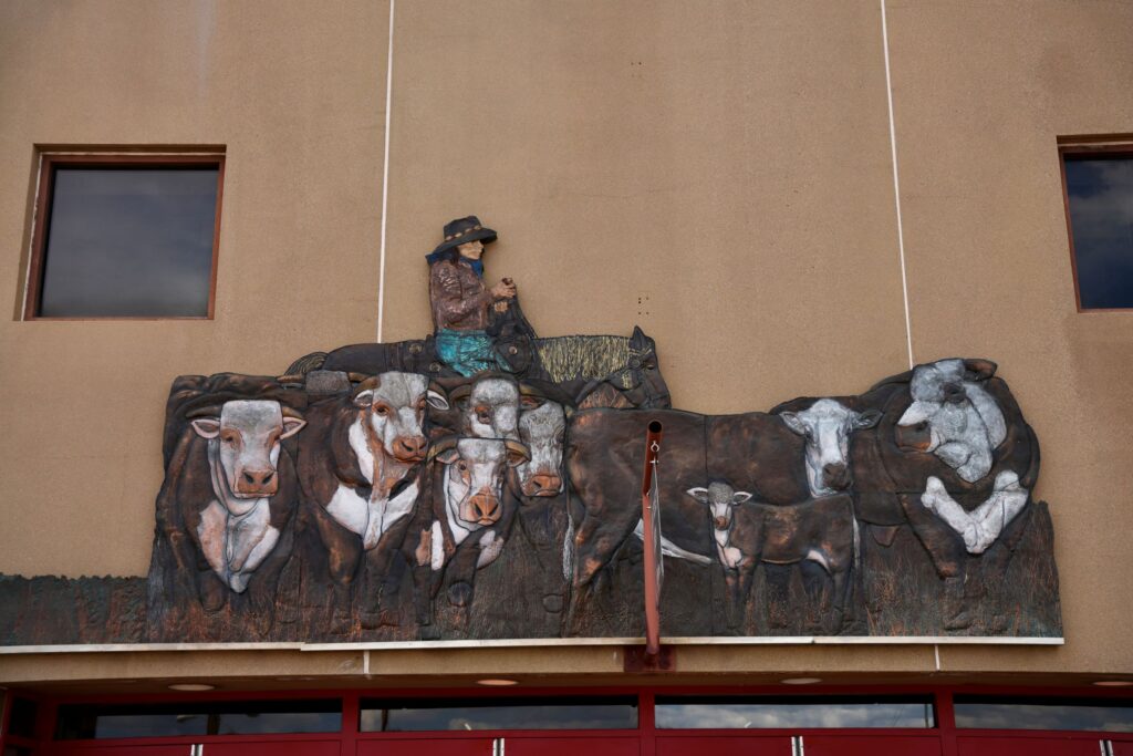 The same bronze relief after restoration, with warm browns and whites bringing out the cattle's faces and a rider in a brown jacket and blue jeans.