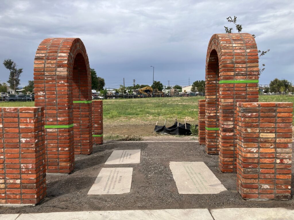 A close view through two red brick arches wrapped with bands of bright green, framing engraved stone pavers set into the ground between them.